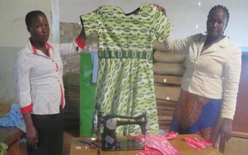 A Survival mother proudly displays her finished dress. Through the skills she learned in the tailoring class, she is able to meet her family's needs.